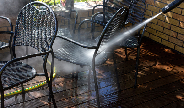 mężczyzna czyszczący myjką ciśnieniową metalowe meble ogrodowe 