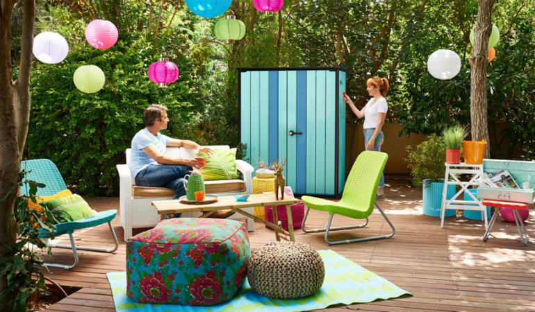 kobieta i meżczyzna odpoczywają na pięknie urządzonym tarasie ze schowkiem ogrodowym, dużo r&oacute;żnych kolor&oacute;w 